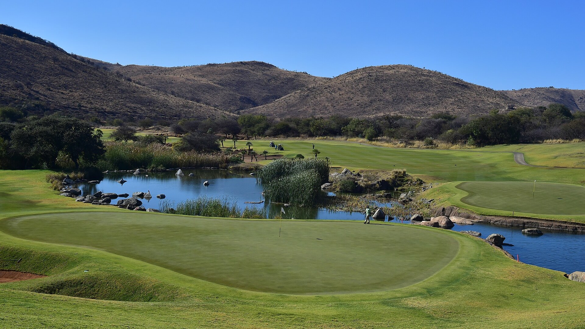 Elevated view over a water-guarded green at the Gary Player Country Club, Sun City, with the Pilanesberg hills behind